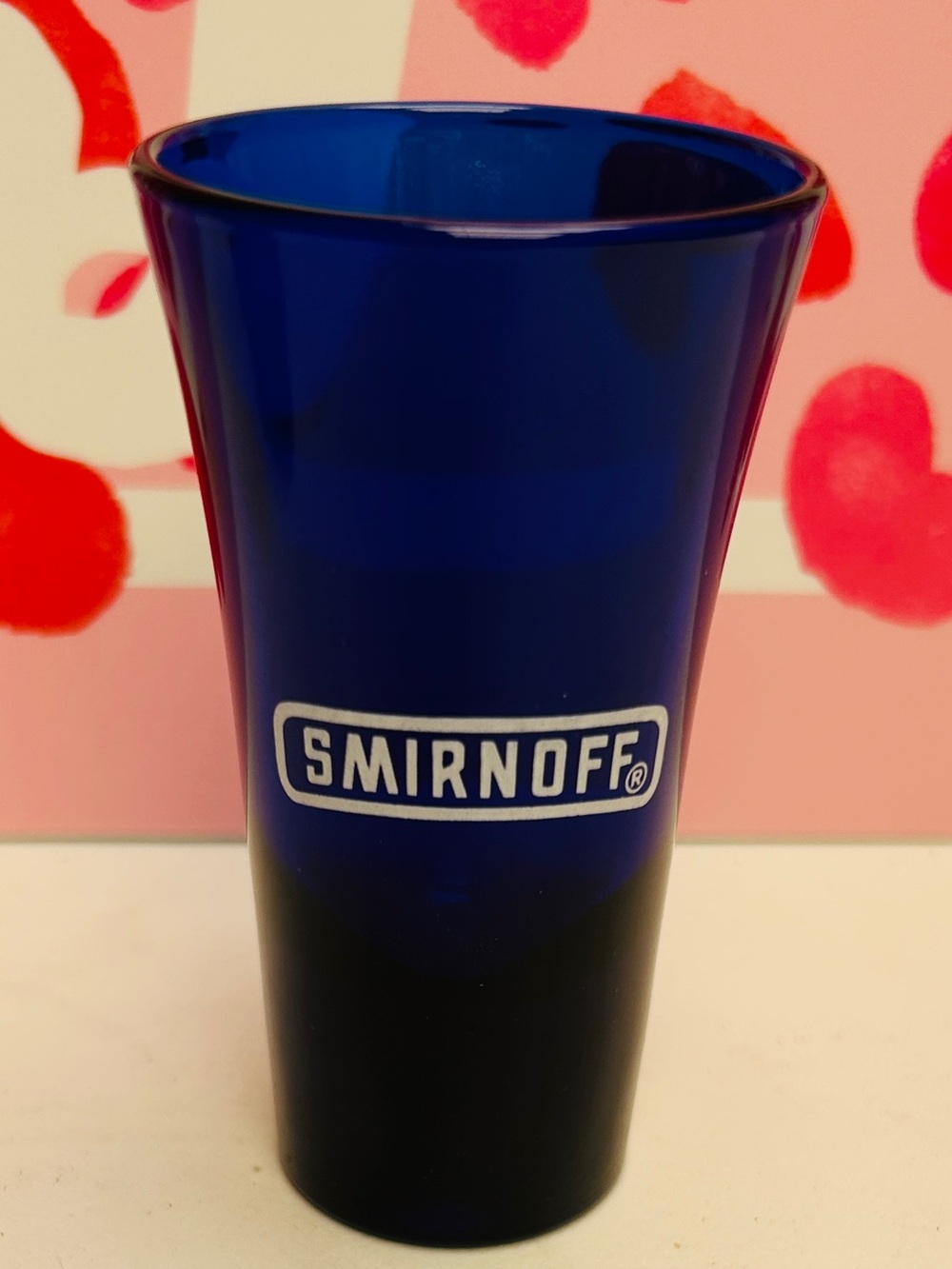 Shot glass, cobalt blue with Smirnoff logo in white.